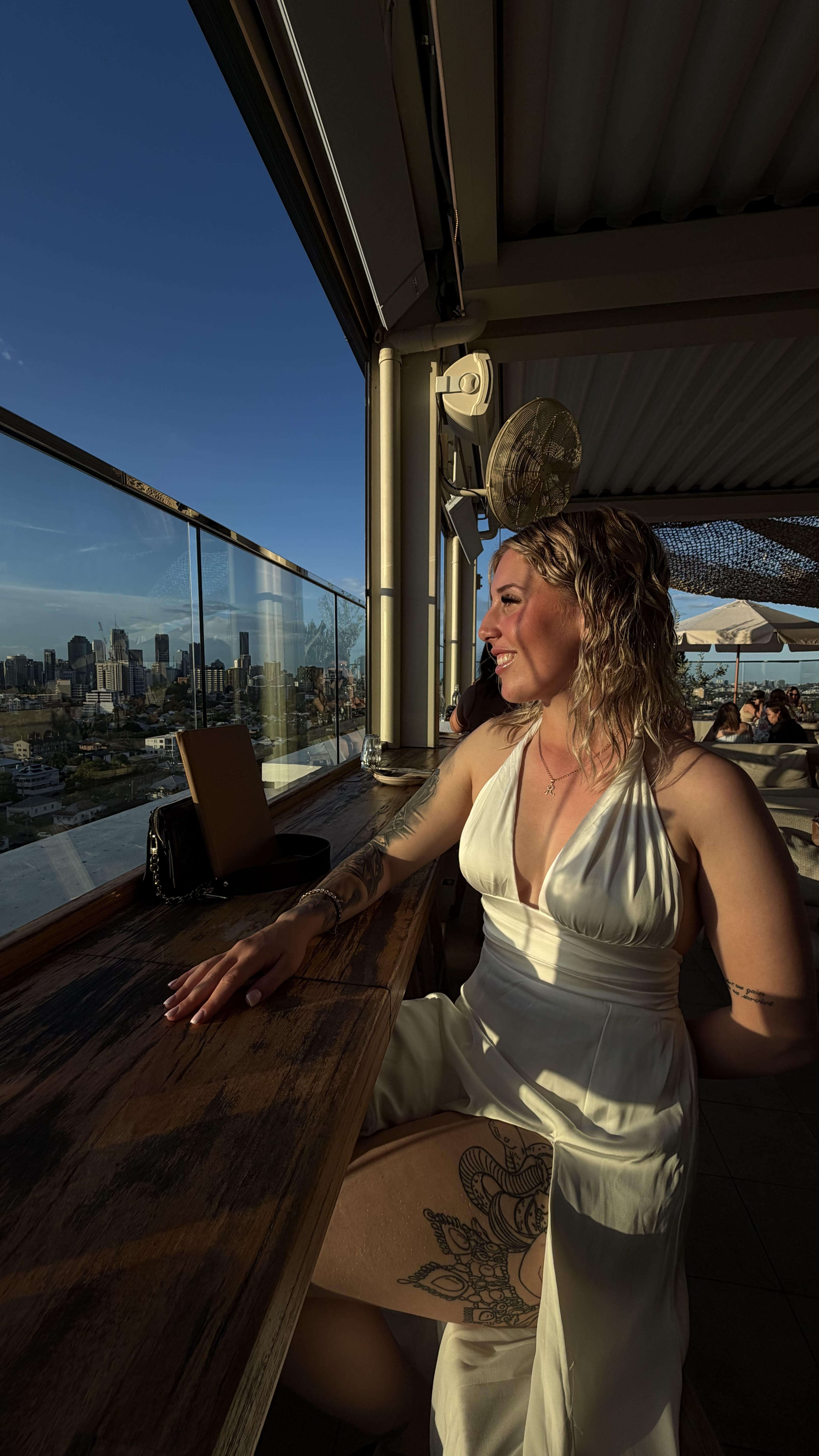 Rileigh Goodrich, CEO of BodyBloom Wellness, standing confidently on a rooftop with city skyline in background during golden hour